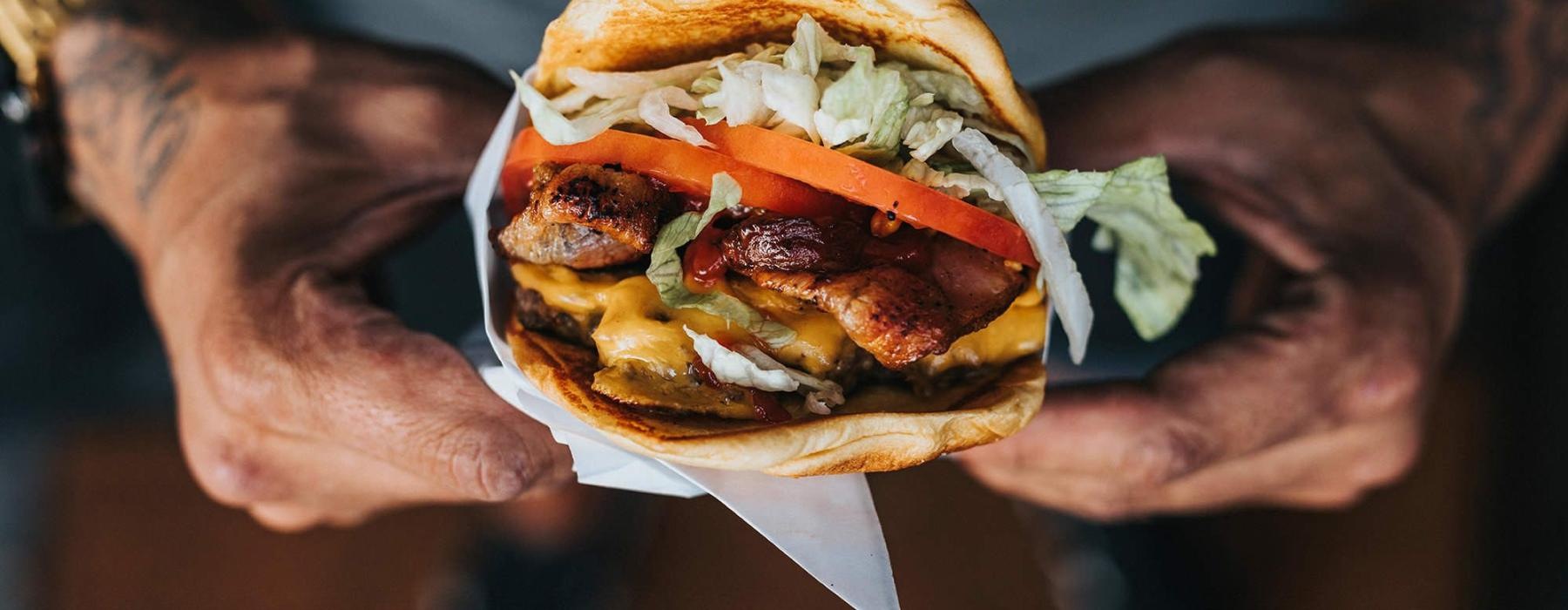 man holds a thick, juicy burger with both hands