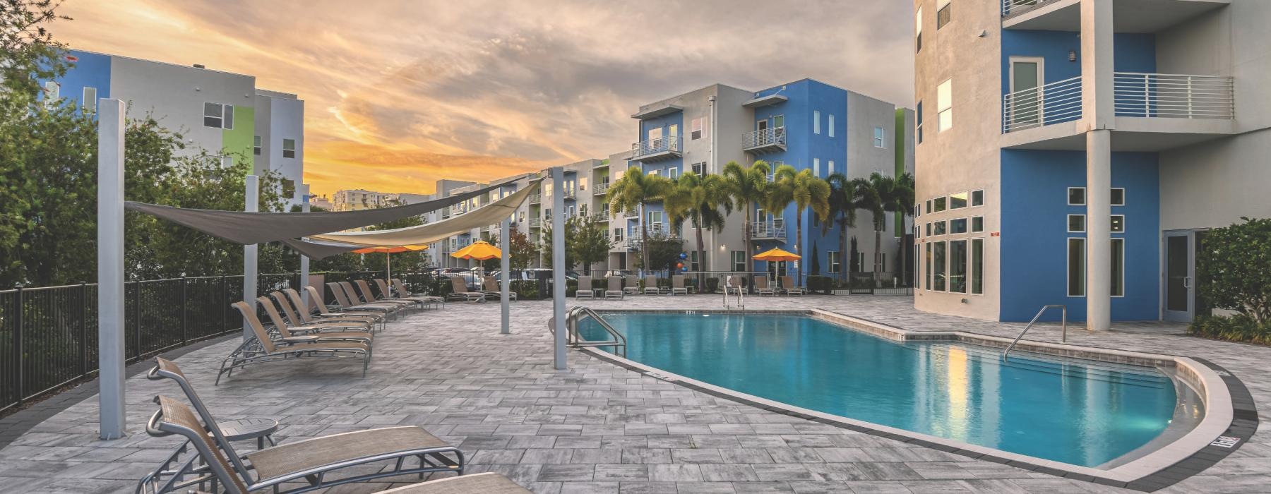 a pool with chairs and a table by it by a building